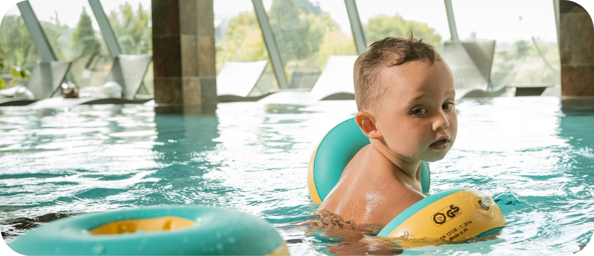 Ein Kind schwimmt im Schwimmbad mit grünen und gelben KraulQuappen an den Händen.